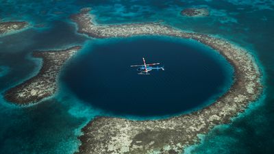 blue helicopter flying over large blue hole